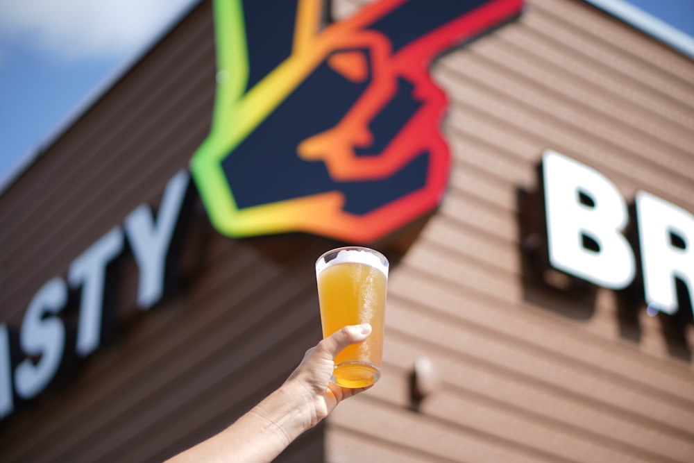 a person holding a glass of beer in front of a building