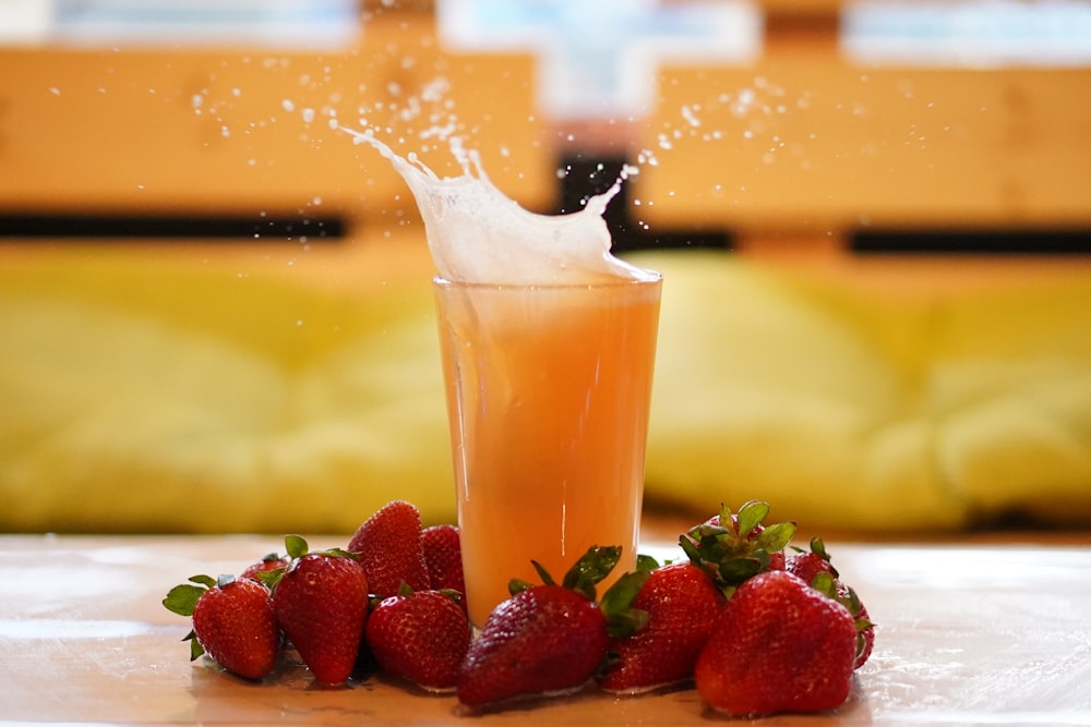 a glass of orange juice and strawberries on a table