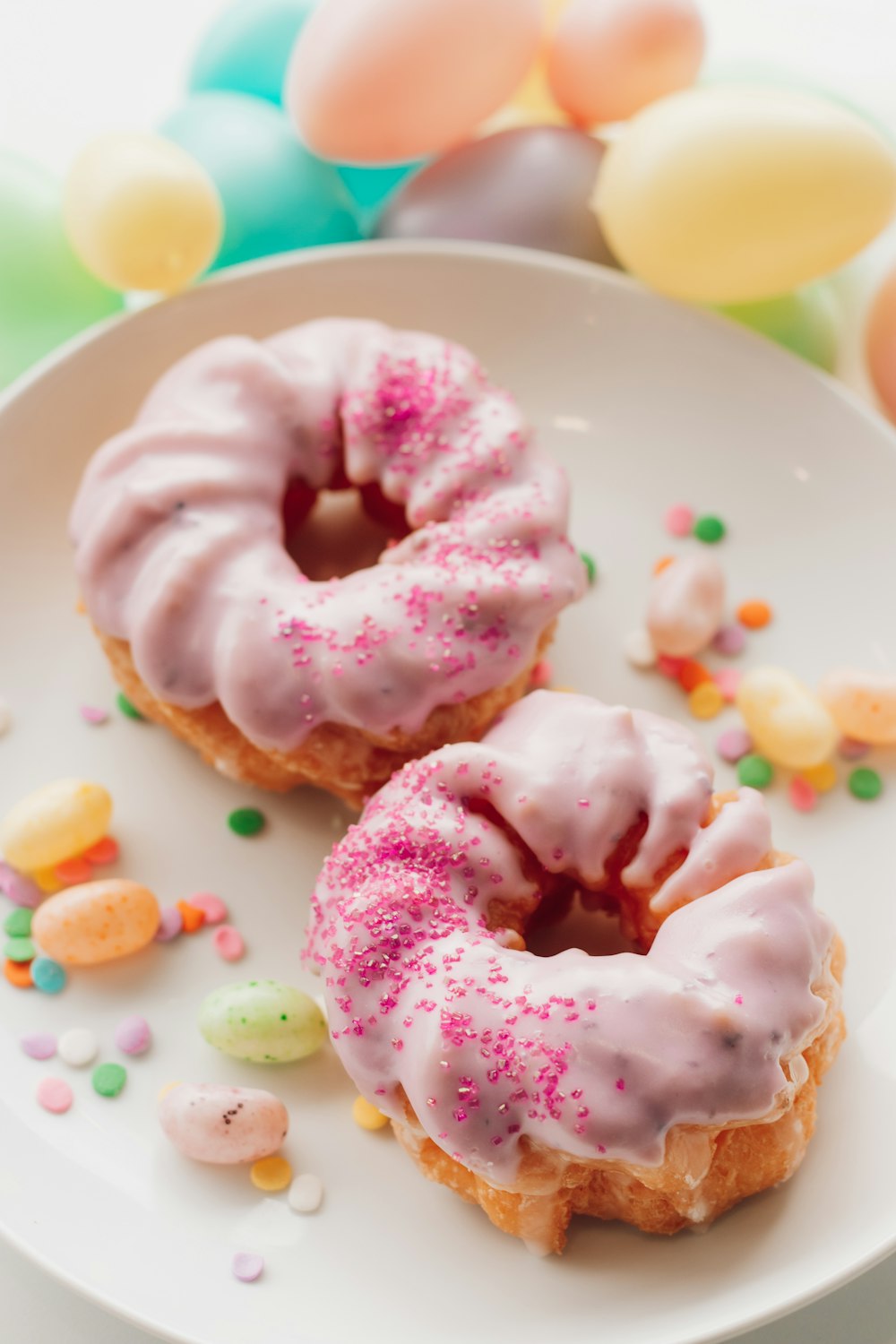 two donuts with pink icing and sprinkles on a plate