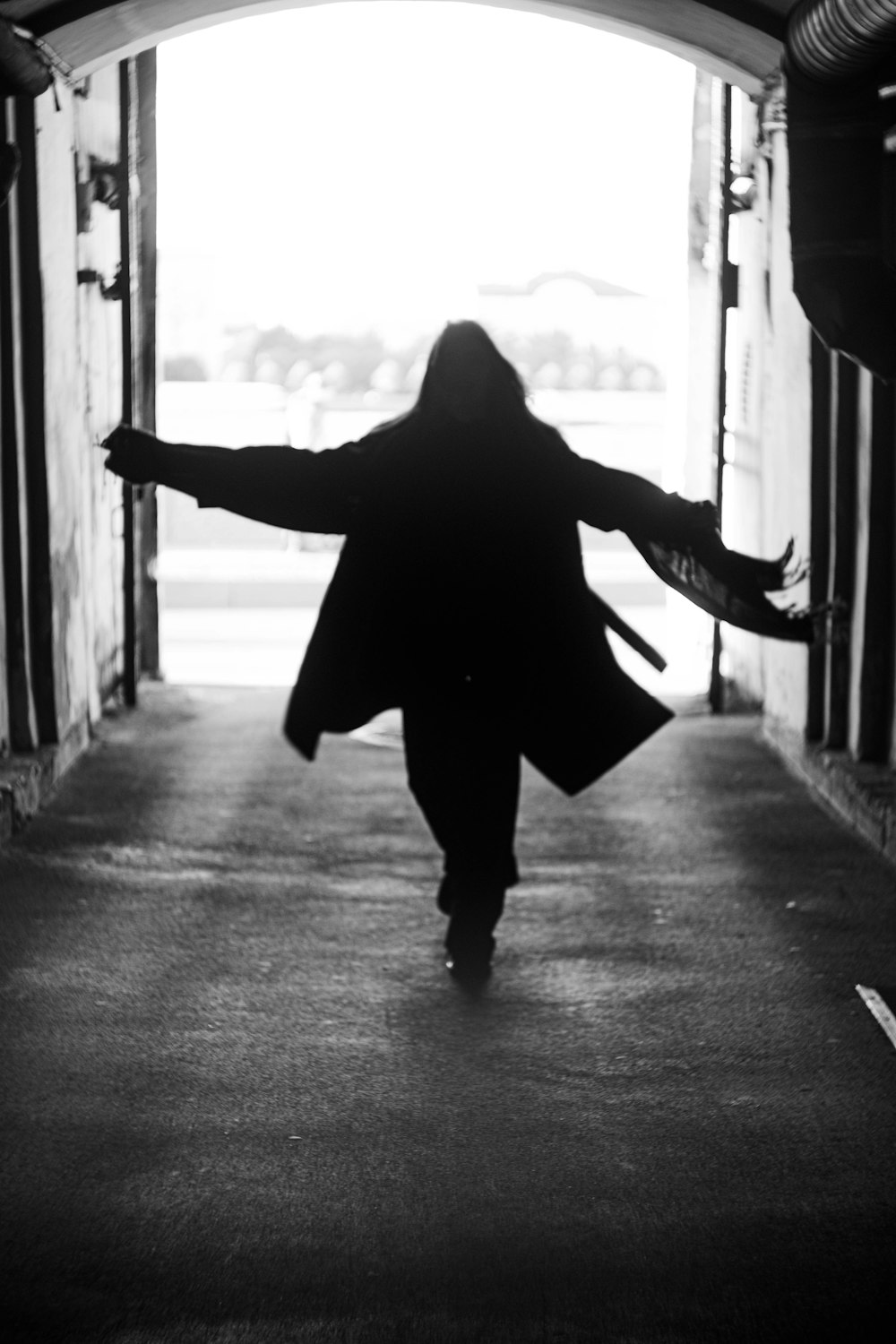 a woman in a long coat is walking out of a tunnel