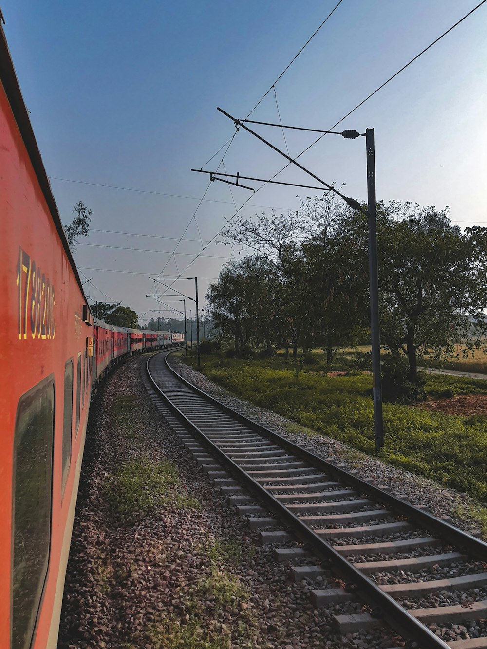 a red train traveling down train tracks next to a lush green field