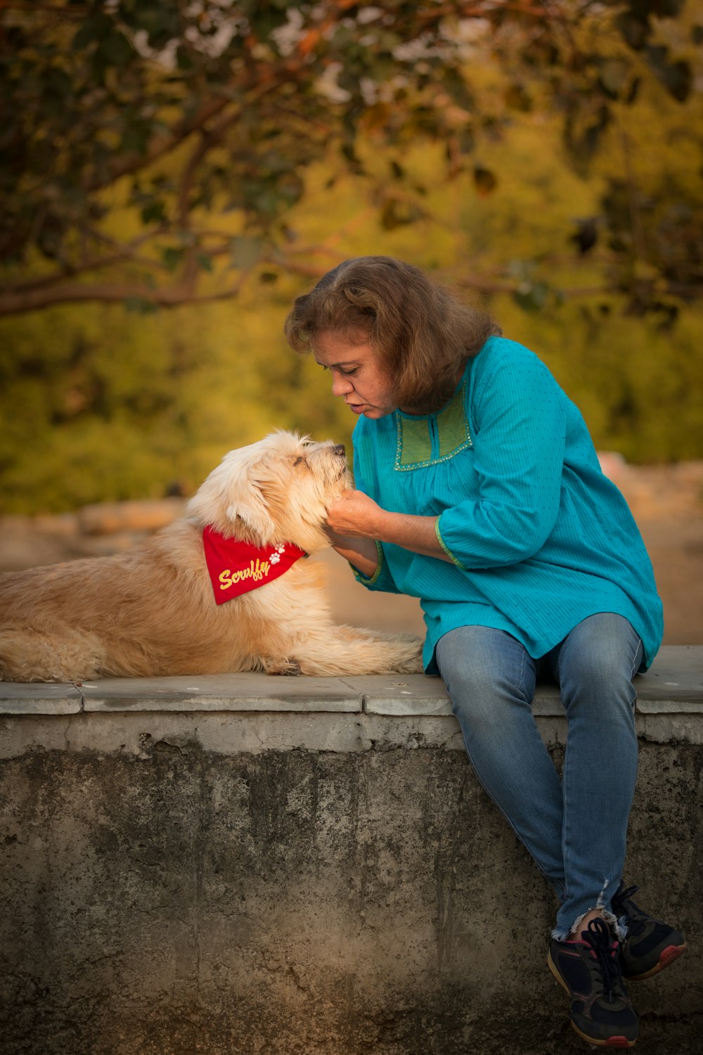 a woman sitting on a ledge petting a dog