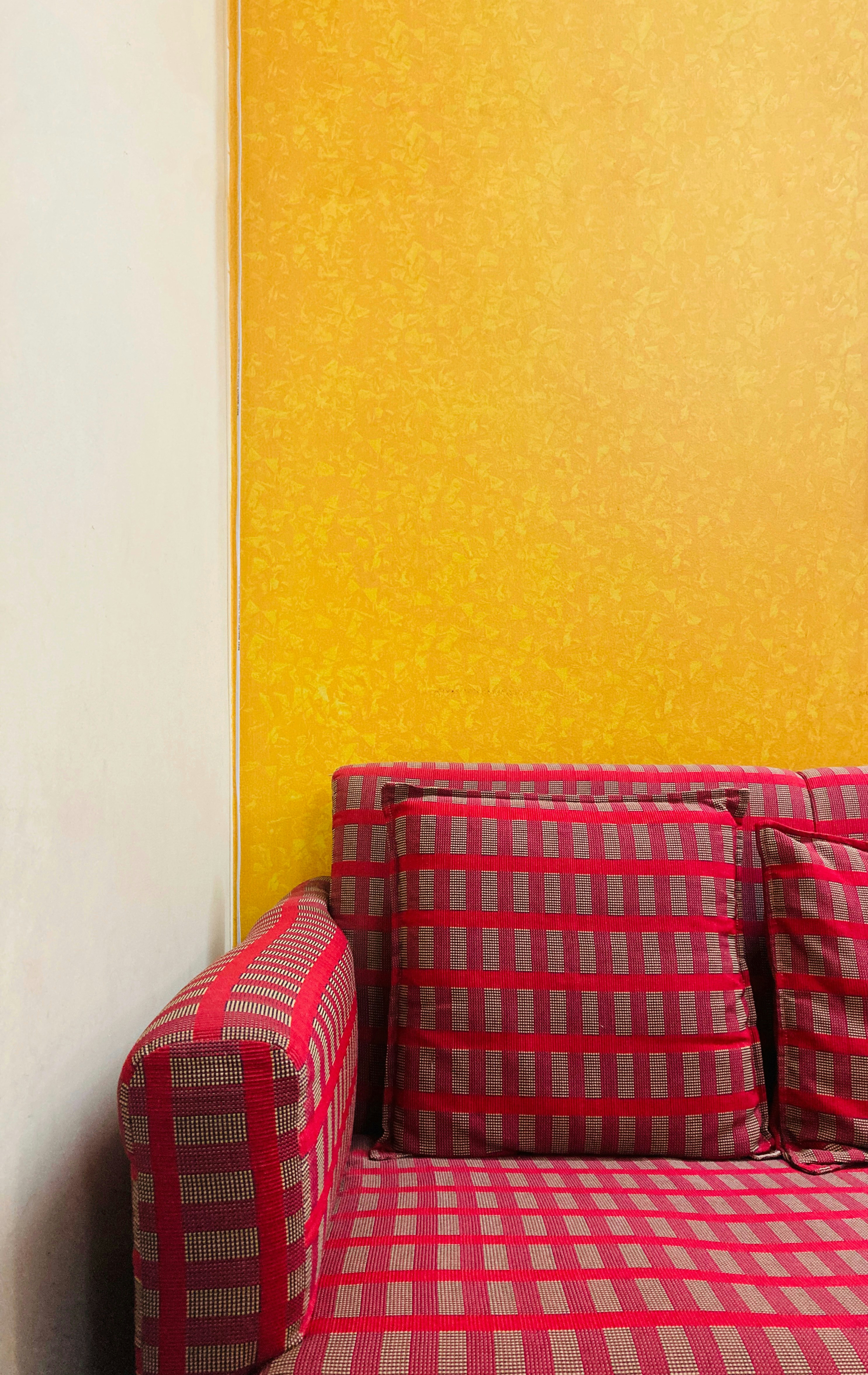 Sofa merah duduk di depan dinding kuning