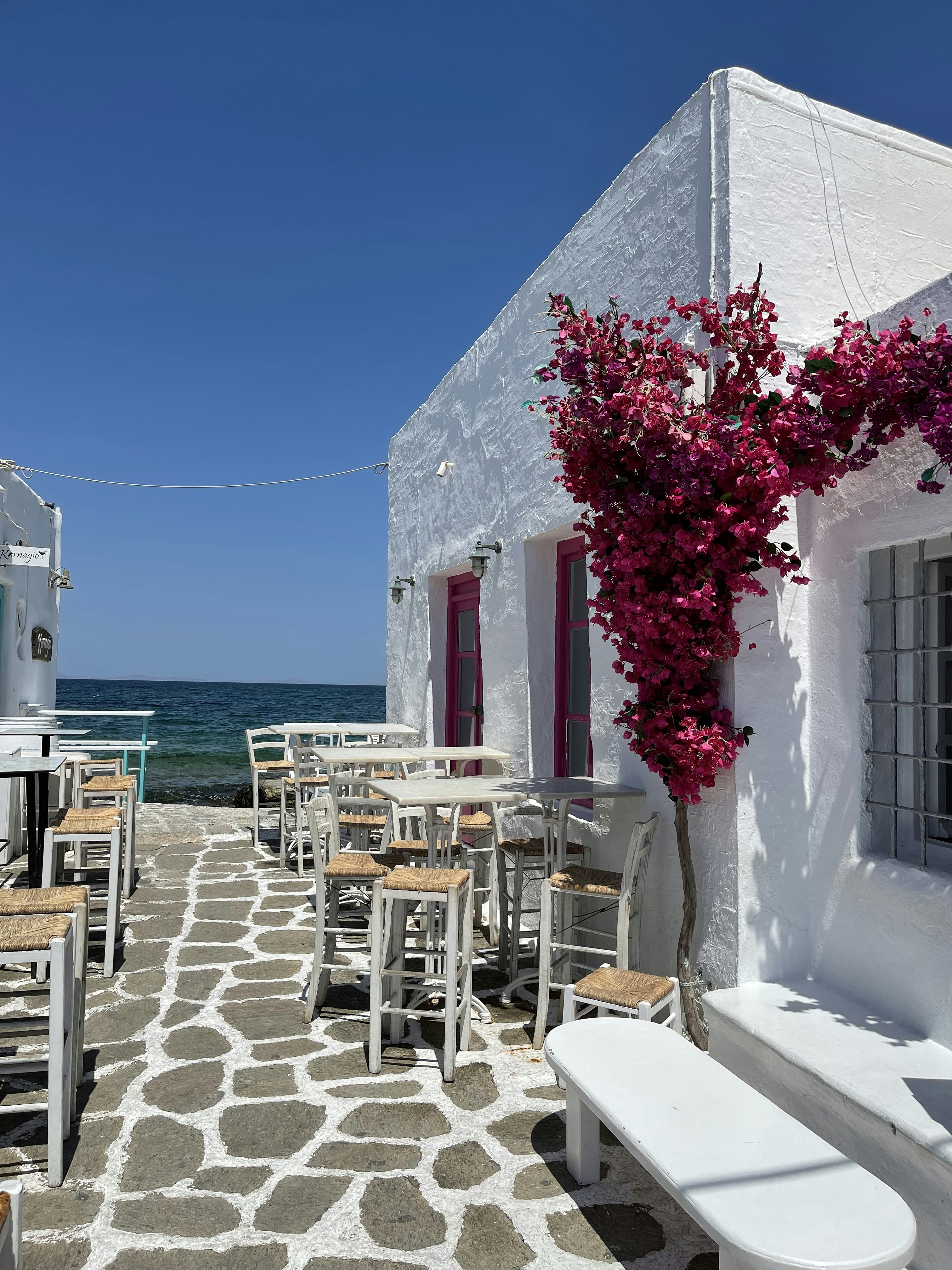 a white building with tables and chairs next to the ocean