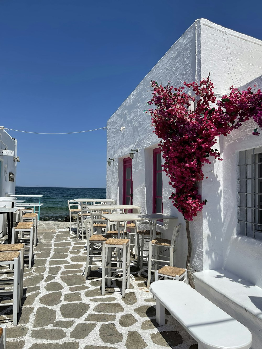 a white building with tables and chairs next to the ocean