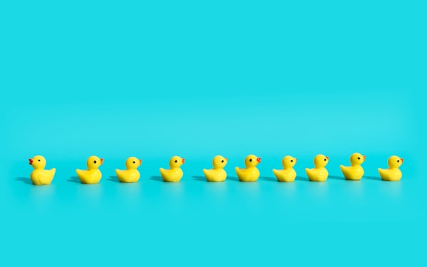 A row of 10 yellow rubby duckies sit on a light blue background.