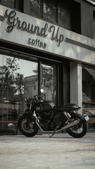 A sleek mobile coffee motorcycle parked in an industrial park setting, with a barista serving a fresh latte.