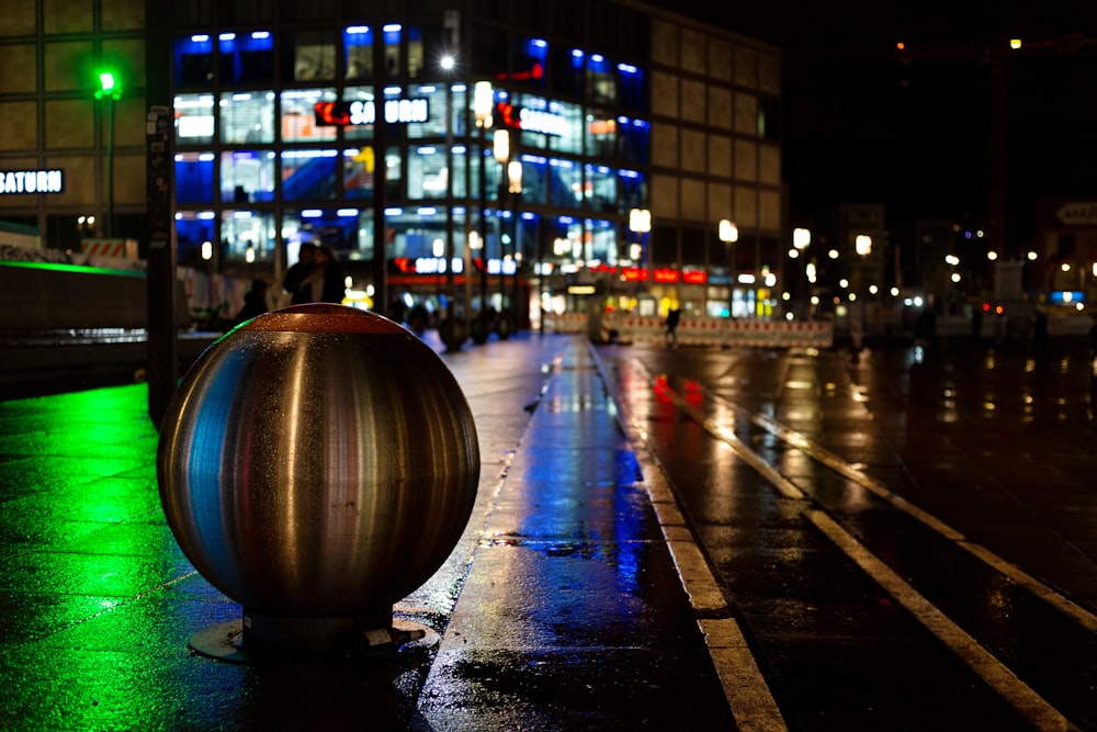 a shiny ball sitting on the side of a wet street
