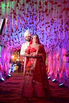 A groom wearing an indo-western coat with rich embroidery, standing against a backdrop of festive lights.