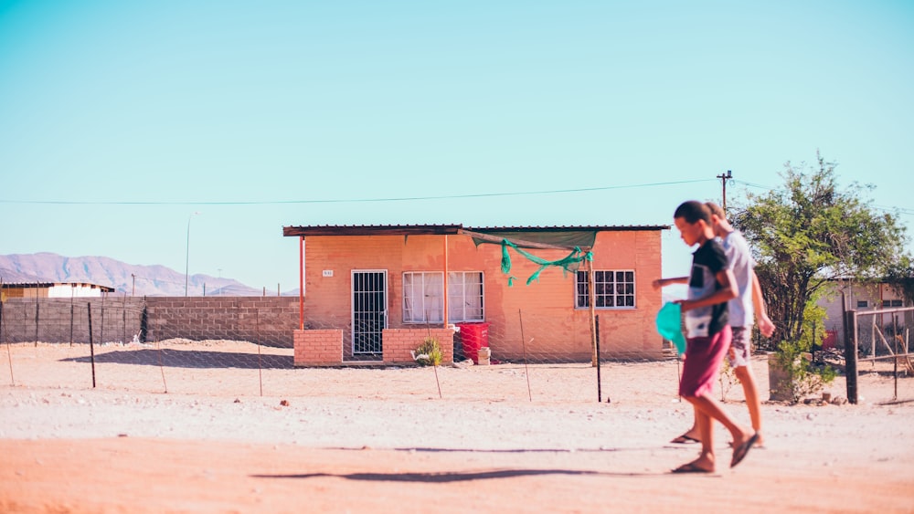 a woman walking across a dirt field next to a building