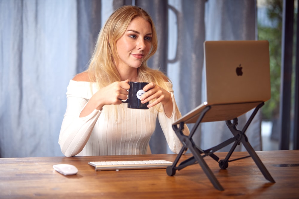 a woman sitting at a table with a laptop and a cup of coffee