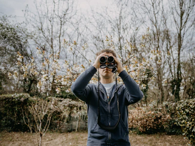 A peaceful scene of a birdwatcher with binoculars standing by a pond at sunrise.