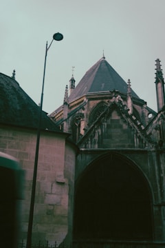 A gothic-style church with intricate architectural details, including pointed arches and a steep roof. A streetlamp stands nearby, silhouetted against the sky, adding a touch of modernity to the historical structure. The image has a muted, moody color palette.