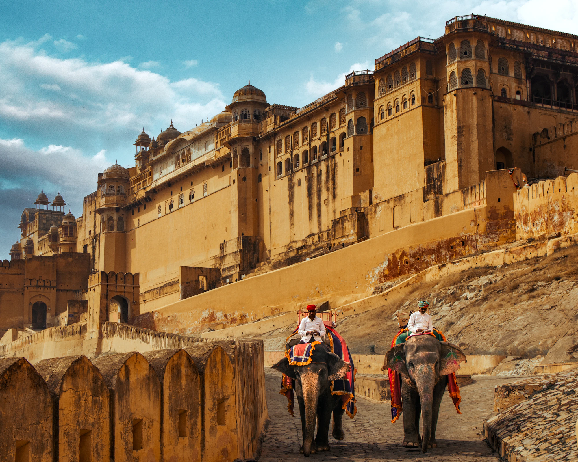 Amer Fort in Jaipur beneath heavy monsoon cloud, with the Aravalli hillside behind the ramparts