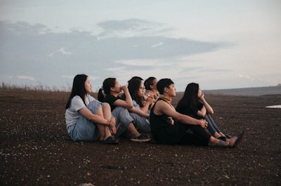 a group of women sitting on top of a dirt field