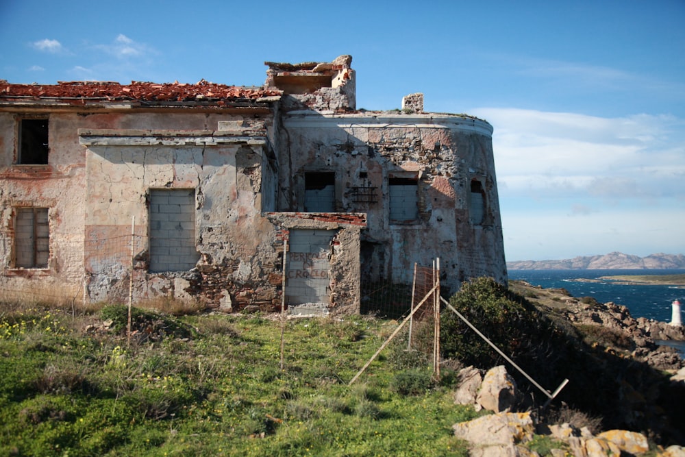 an old run down building sitting on top of a hill next to a body of