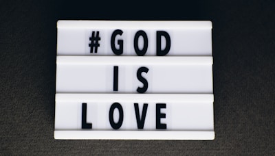 A lightbox sign featuring black uppercase letters spelling out '#GOD IS LOVE' on a white background, set against a dark surface.