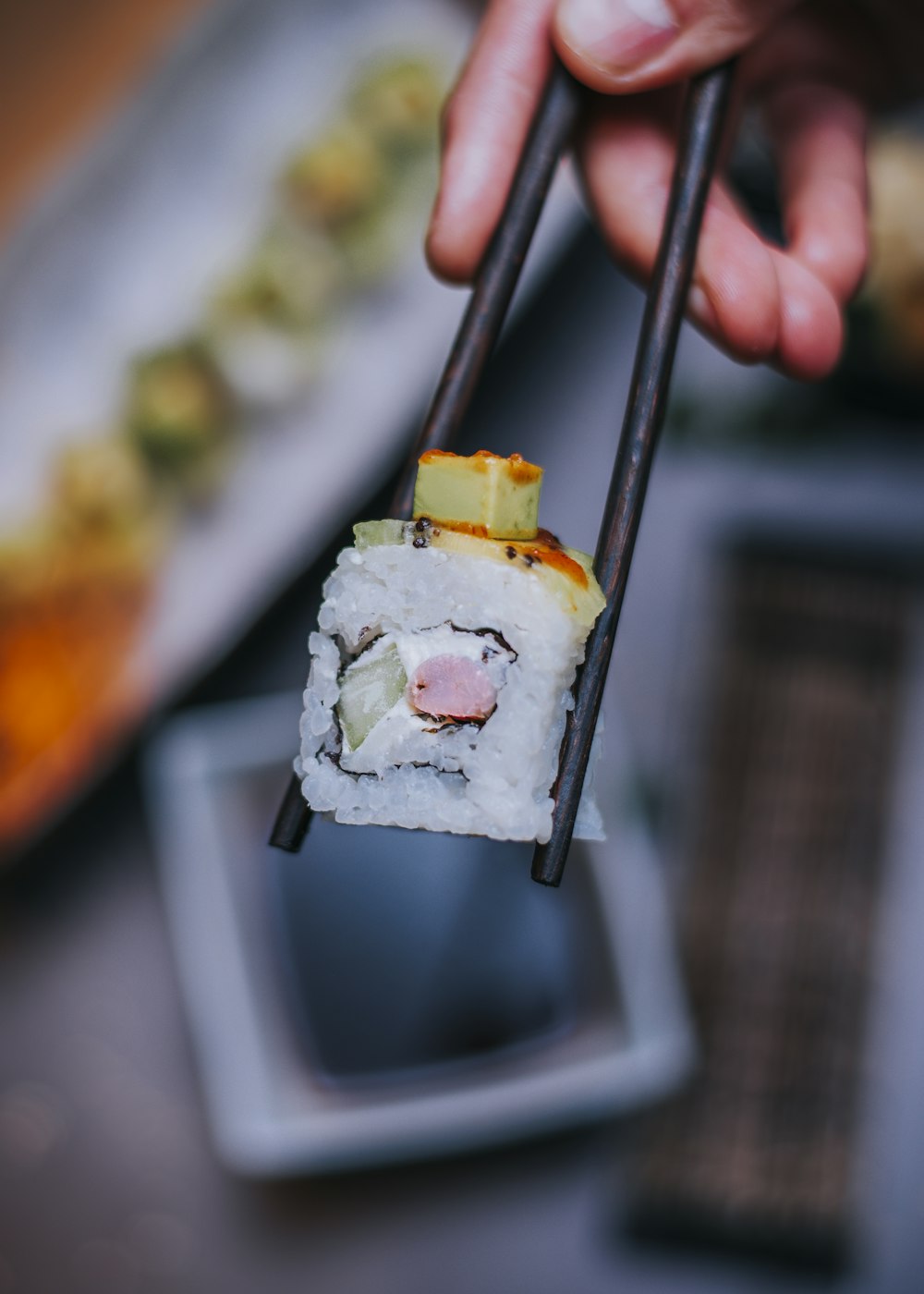 a person holding a piece of sushi with chopsticks