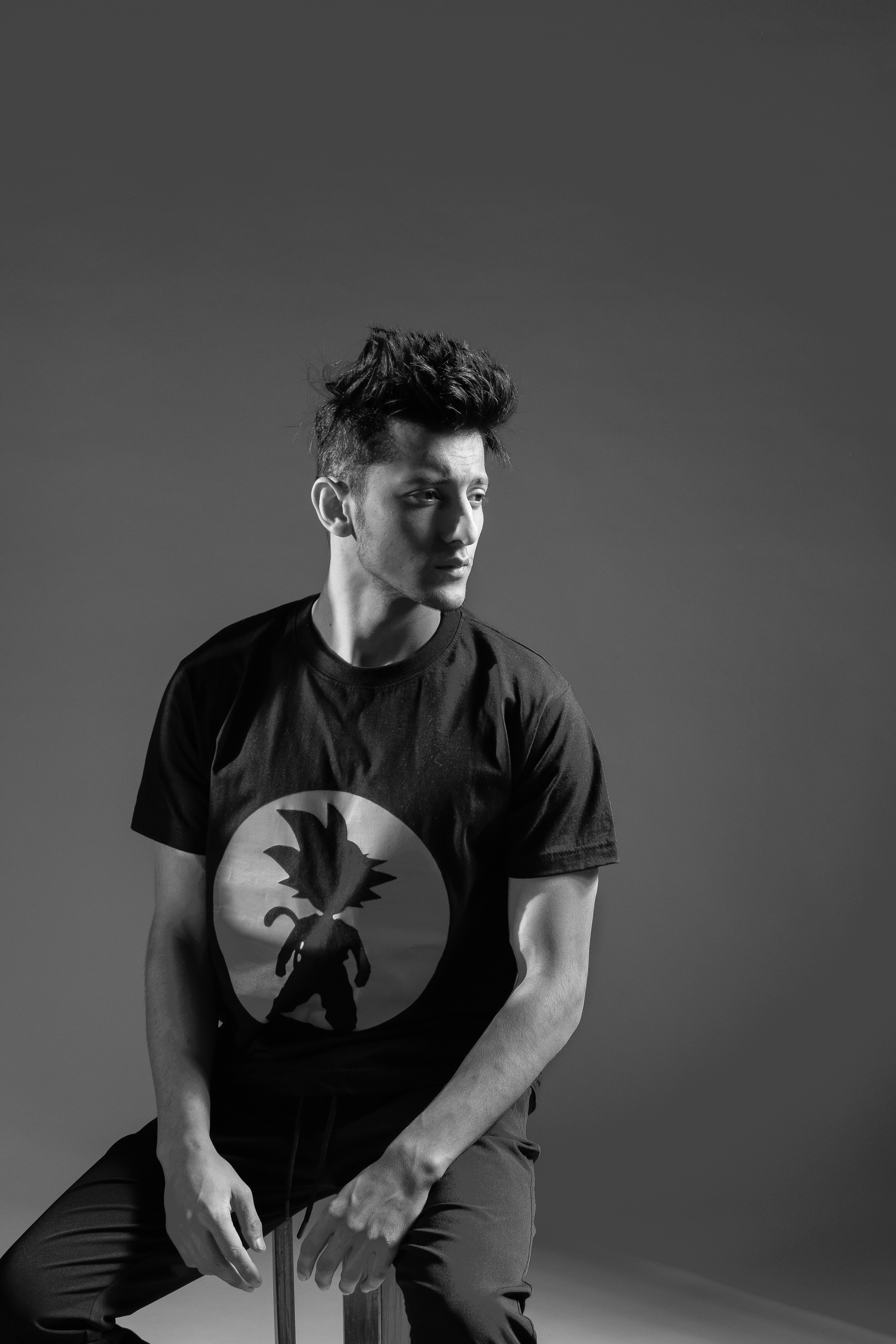 Male model in tailored pants and graphic tee, dark editorial background, shadow play