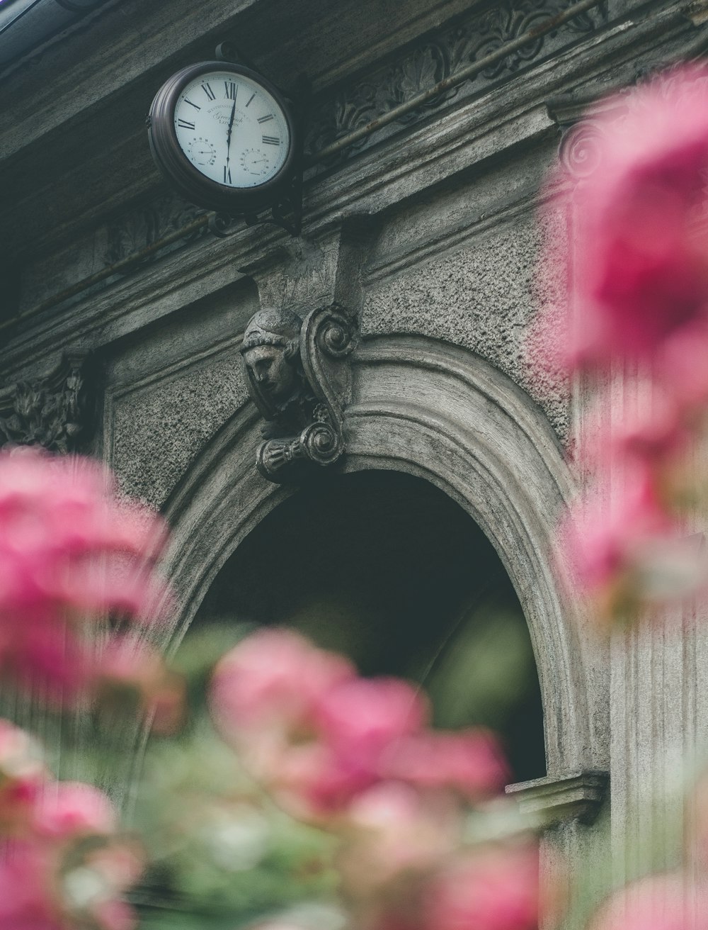 a clock on the side of a building with pink flowers