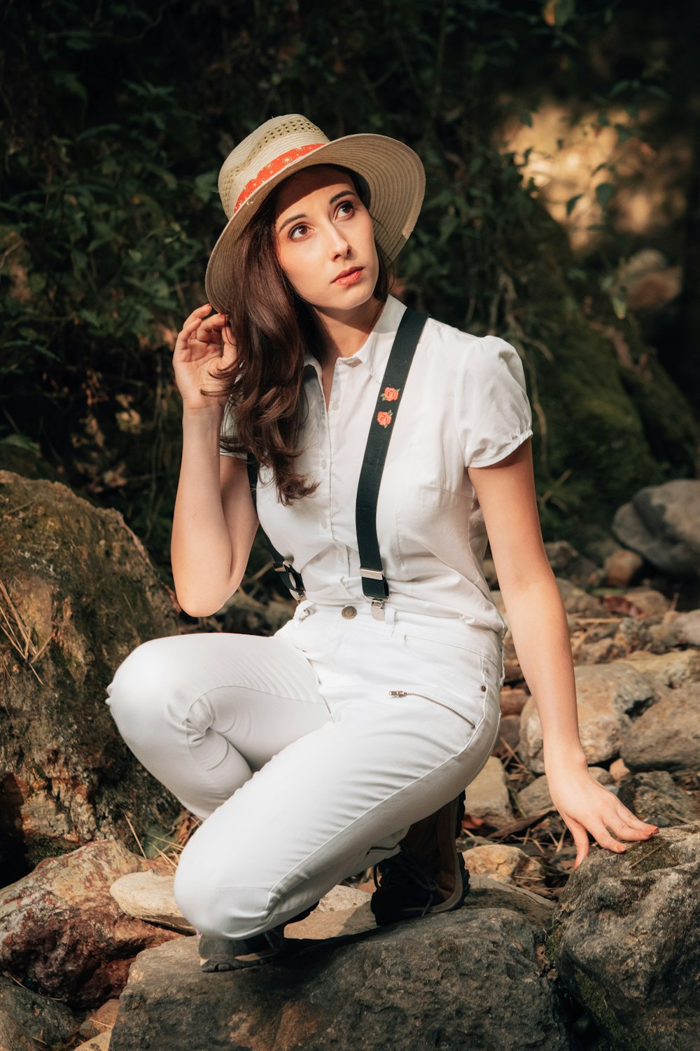 a woman in a hat is sitting on a rock