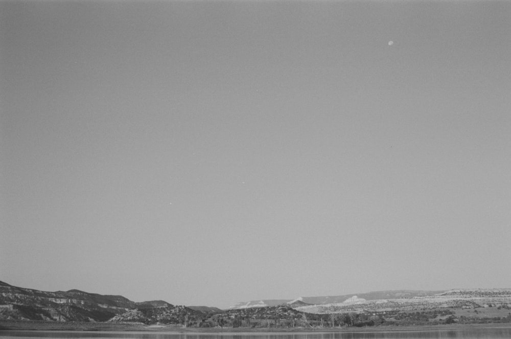 uma foto em preto e branco de um lago com montanhas ao fundo