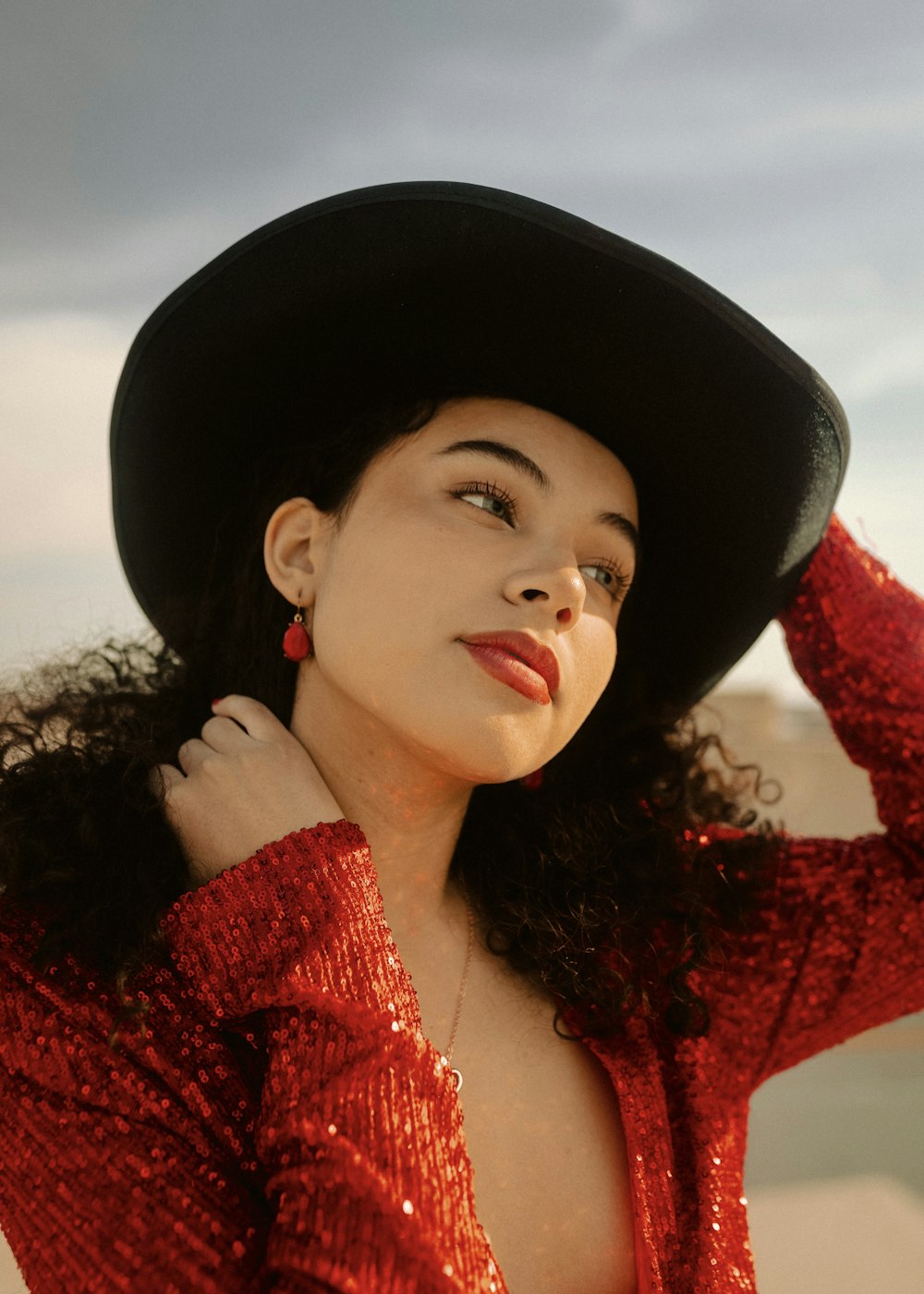 a woman wearing a red sequin dress and a black hat