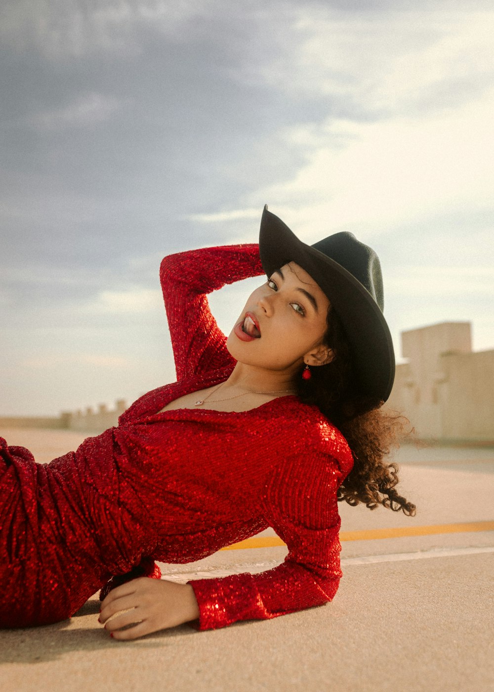 a woman in a red dress and black hat laying on the ground