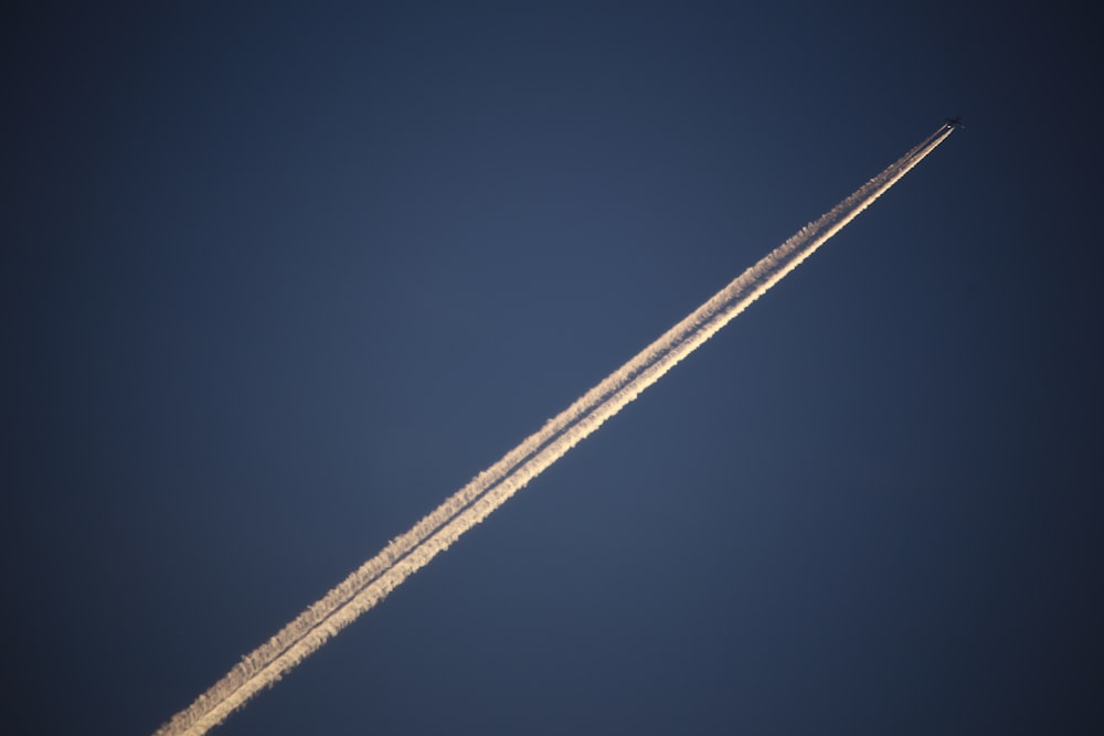 a jet flying through a blue sky with a contrail