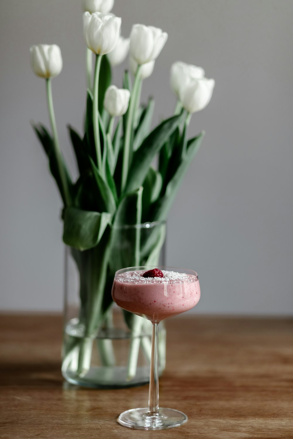 a pink drink in a glass next to a vase of tulips