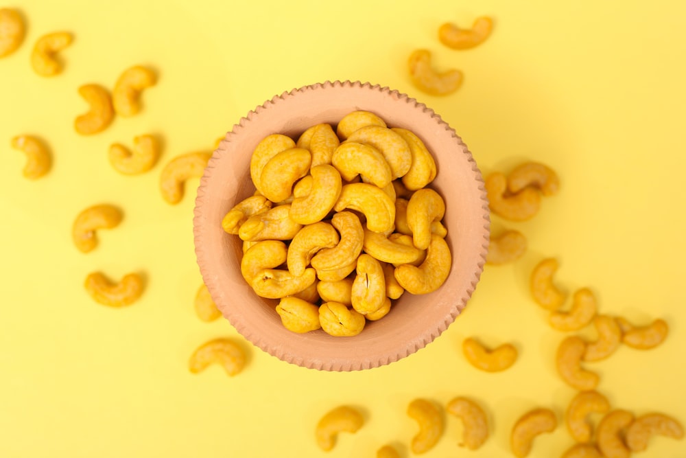 a pink bowl filled with cashews on a yellow background