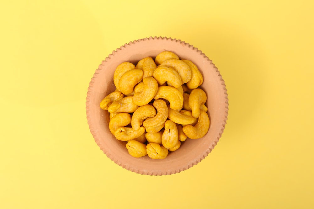 a pink bowl filled with cashews on a yellow background
