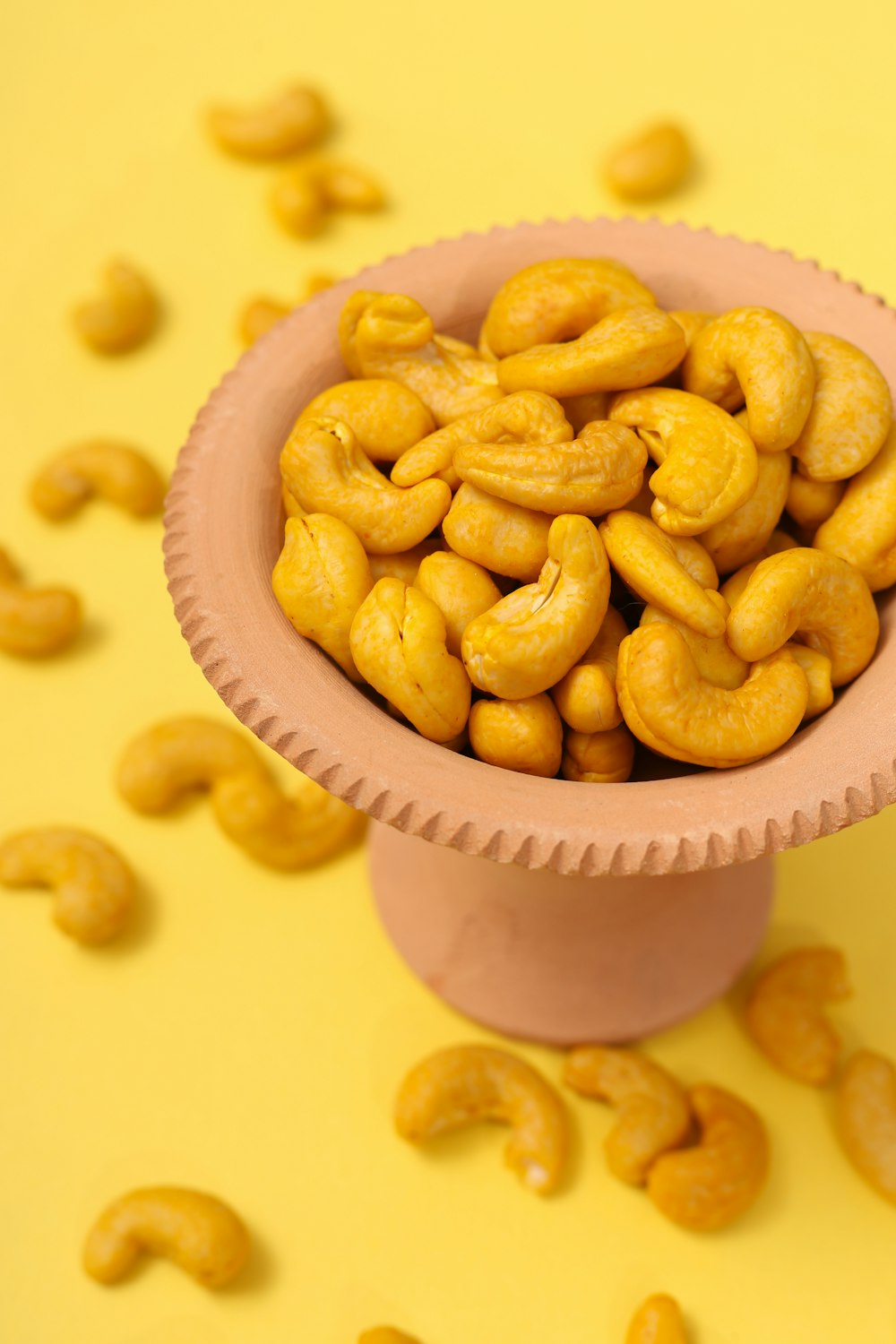 a pink bowl filled with cashews on top of a yellow table