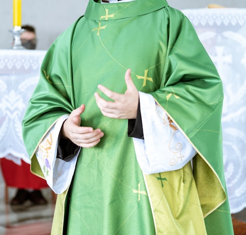 a man in a priest's outfit standing in front of a cross