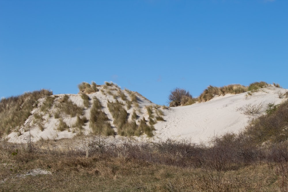 a hill covered in sand and grass under a blue sky