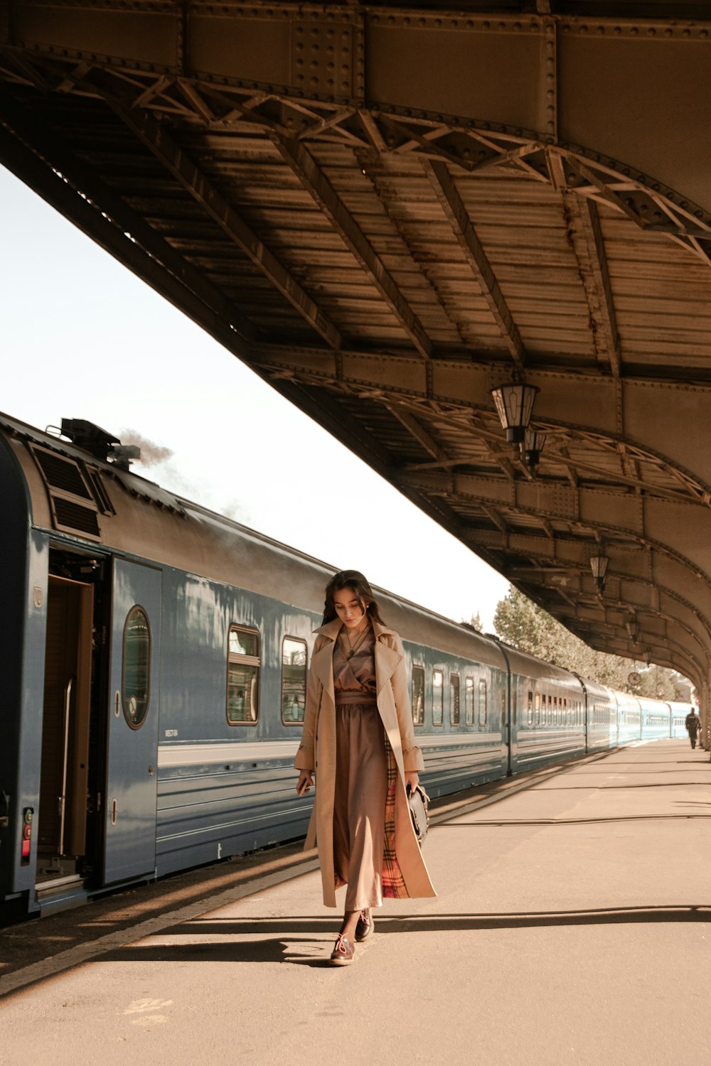 a woman in a trench coat is walking towards a train