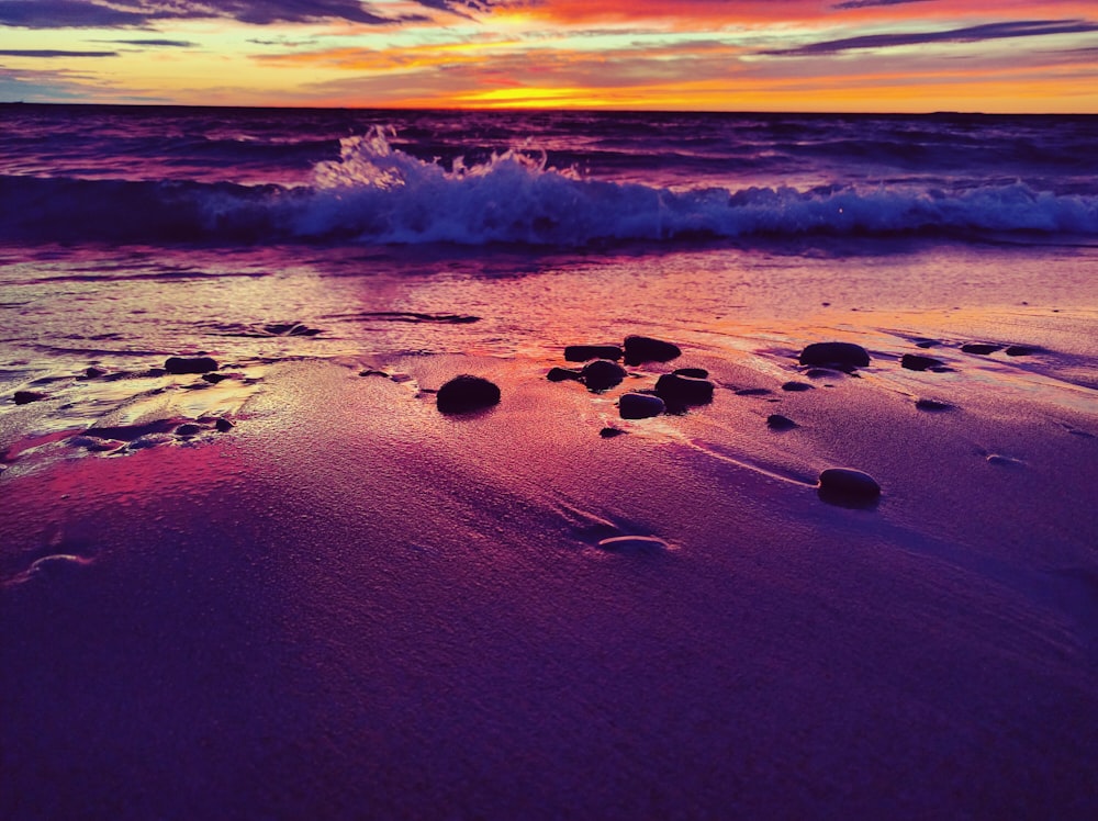 a sunset on a beach with rocks in the sand