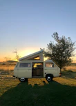 a van parked in a field with the sun setting in the background