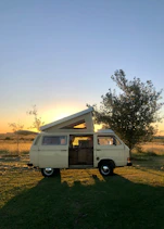 a van parked in a field with the sun setting in the background