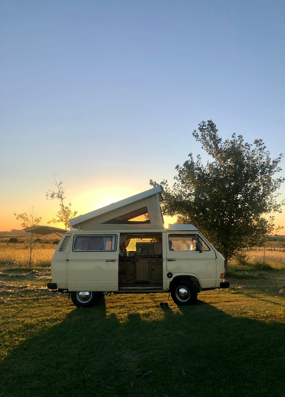 a van parked in a field with the sun setting in the background