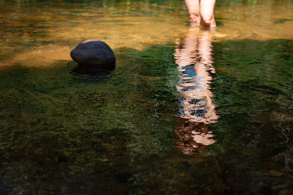 a person walking across a river next to a rock