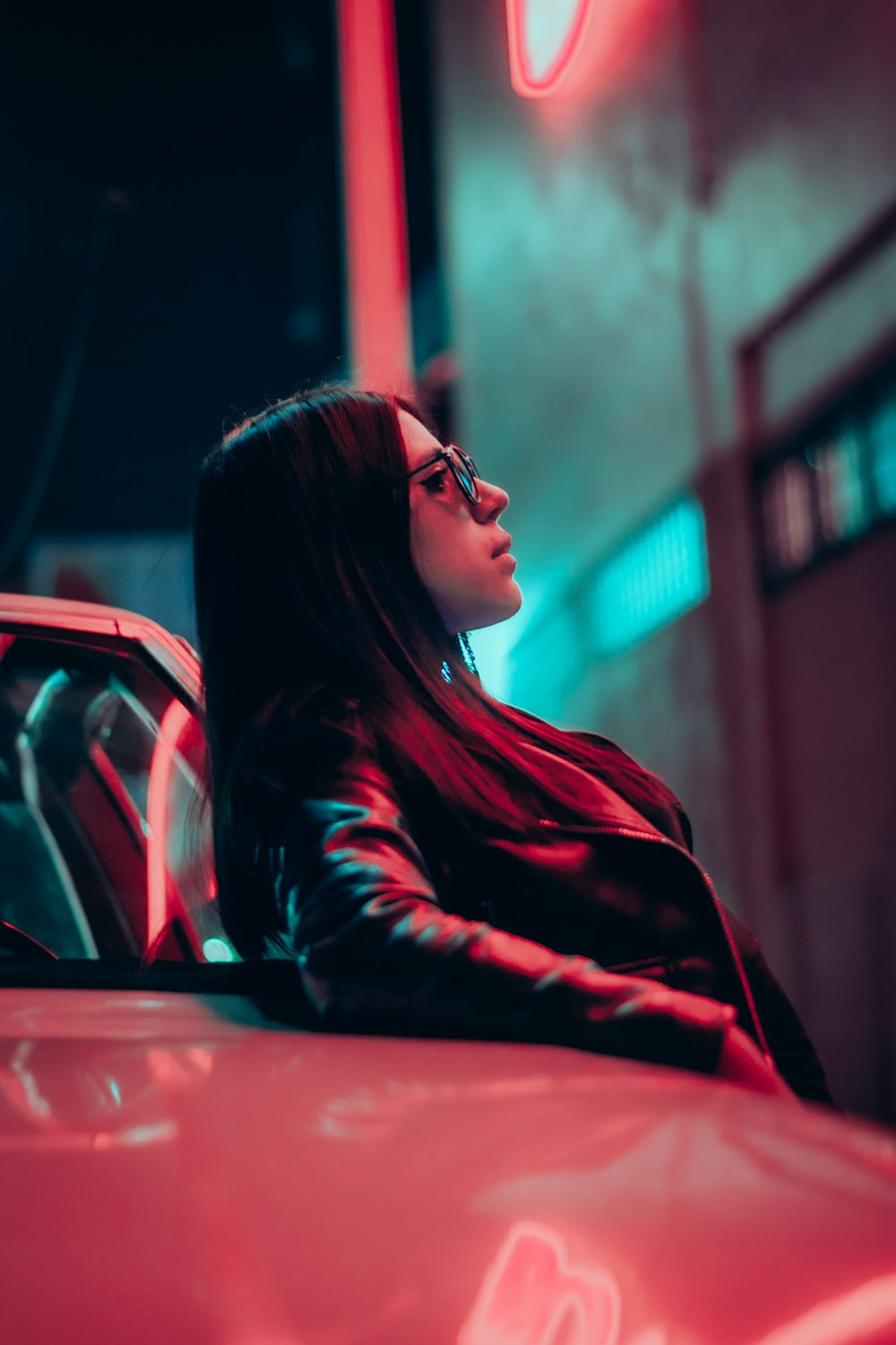a woman in a leather jacket leaning on a red car