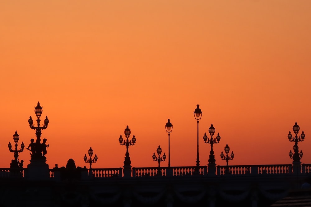 the sun is setting over a bridge with street lamps