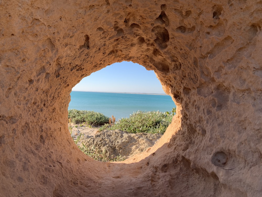 a view of a body of water through a hole in a rock
