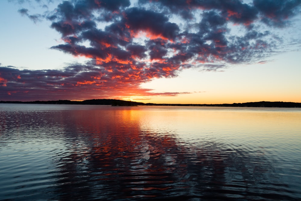 the sun is setting over a calm lake