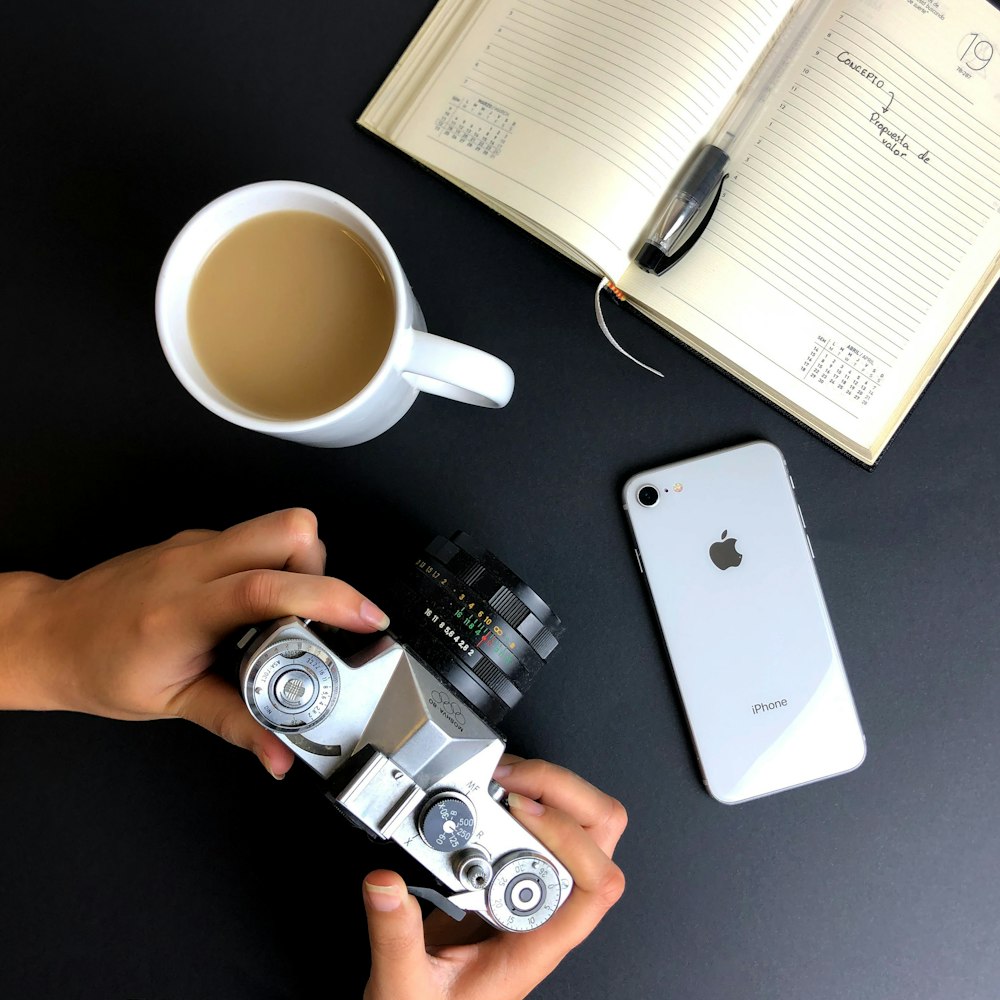 a person holding a camera next to a cup of coffee