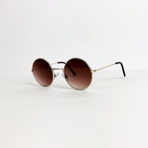 A pair of round sunglasses with a gold frame and brown-tinted lenses is placed on a light, neutral background. The thin arms of the glasses extend elegantly, suggesting a lightweight design.