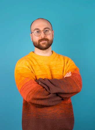 a man with a beard and glasses standing with his arms crossed