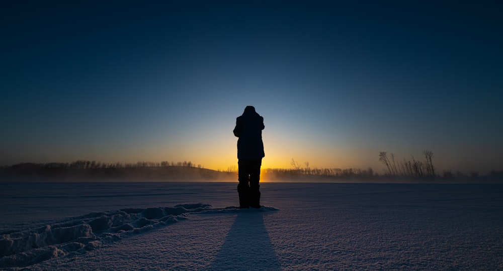 a person standing in the snow at sunset