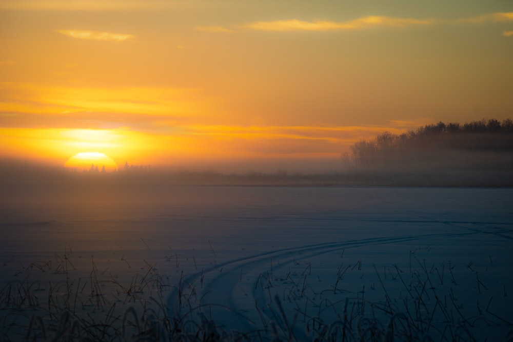 the sun is setting over a frozen lake